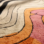 Close-up of a textured rug with wavy patterns in beige, orange, and pink.