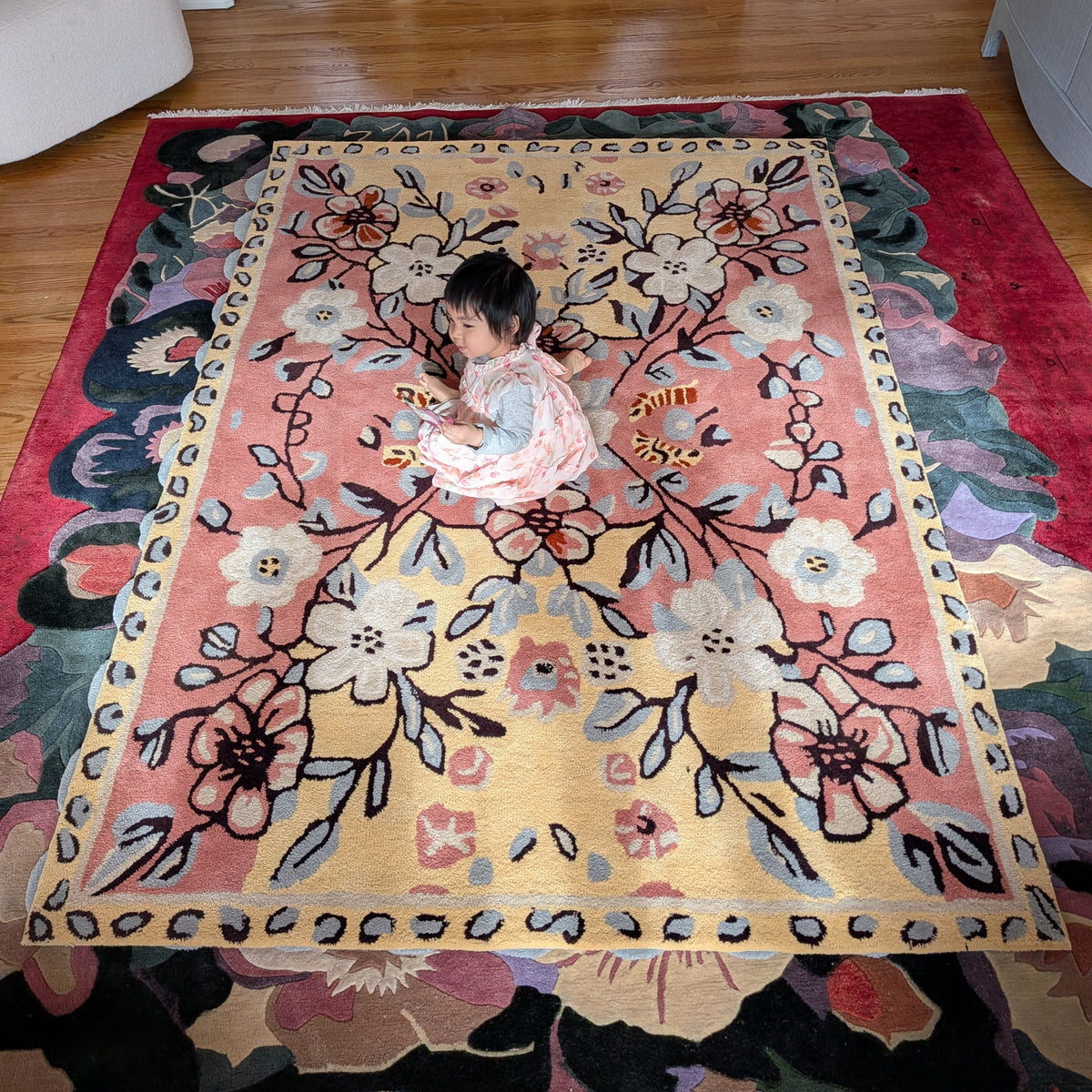 Child playing on a large floral rug in a room with wooden flooring.