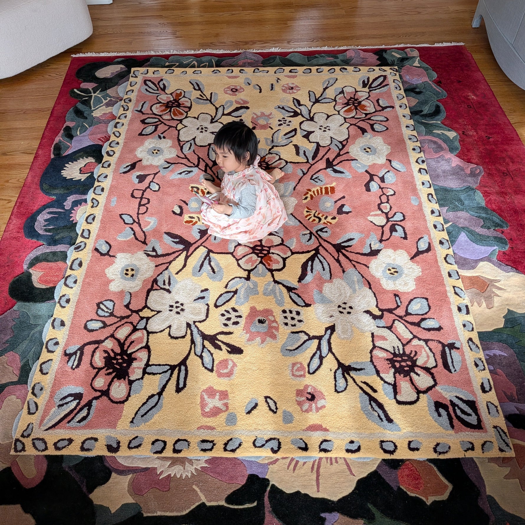 Child playing on a large floral rug in a room with wooden flooring.