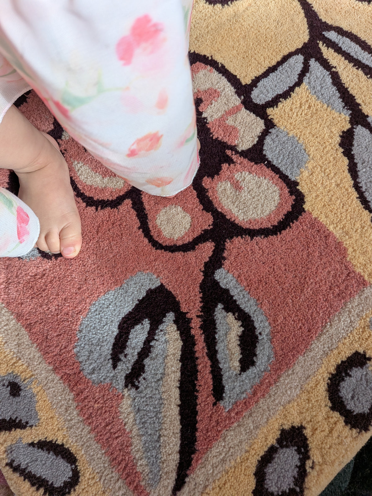 Close-up of a child's feet on a patterned rug with floral designs.