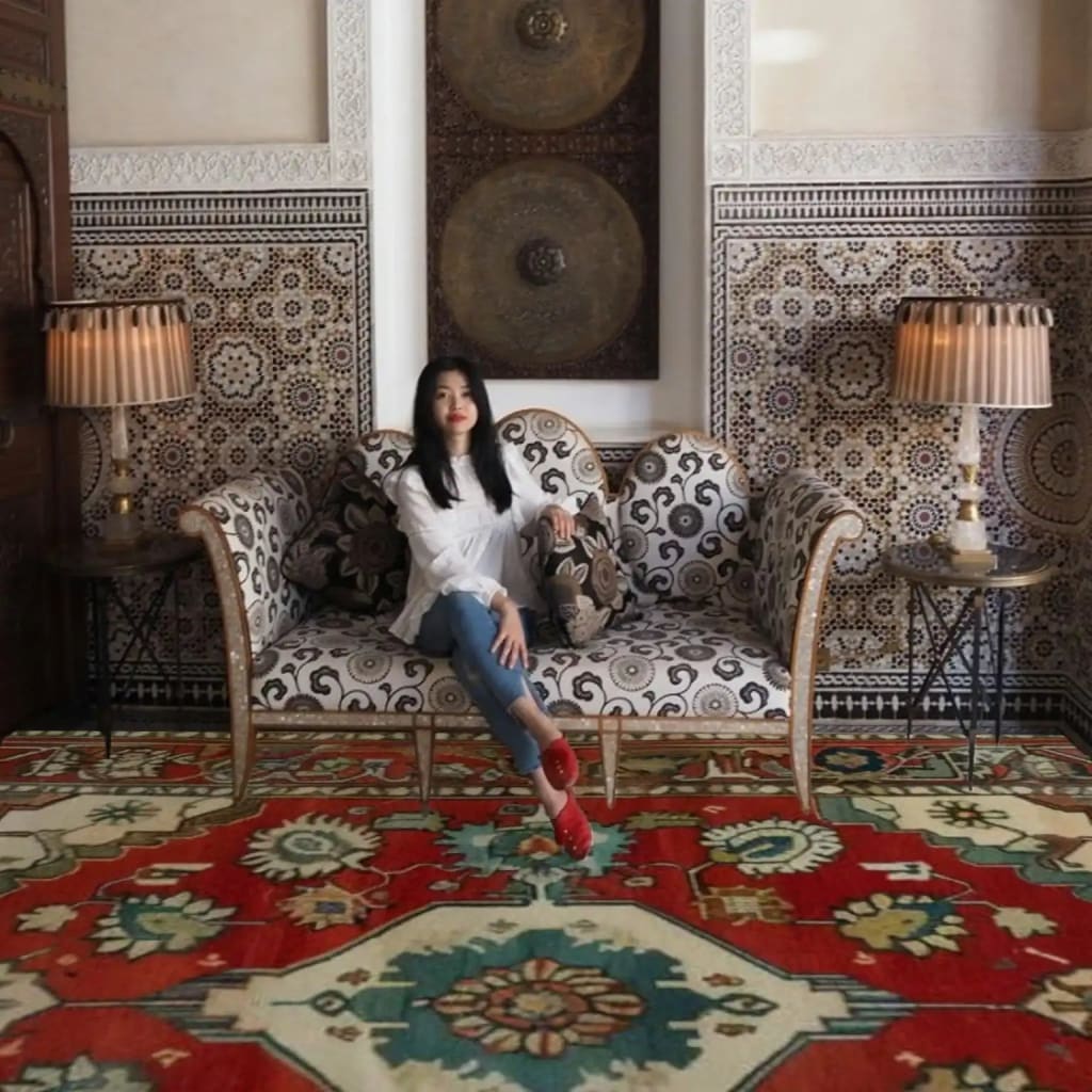 Woman sitting on a patterned sofa in a room with decorative tiles and a large red persian floral rug.