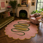 A pink scalloped area rug featuring a large black and gold snake design, styled in a cozy, vintage-inspired living room with a green sofa, pink armchair, and wooden parquet flooring.