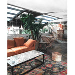 A cozy living room featuring a Royal Majesty Hand Tufted Area Rug with a vibrant floral design, perfect for large living rooms or formal dining rooms. The wool rug adds a touch of elegance to the space, complemented by a comfortable orange sofa and wicker furniture.