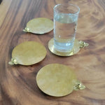Set of four round gold brass Rumduol flower coasters on wood-grain tray, one supporting a tall water glass, showing 3D blossom detail