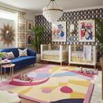 Modern nursery with colorful rug, blue sofa, and abstract art on patterned walls.