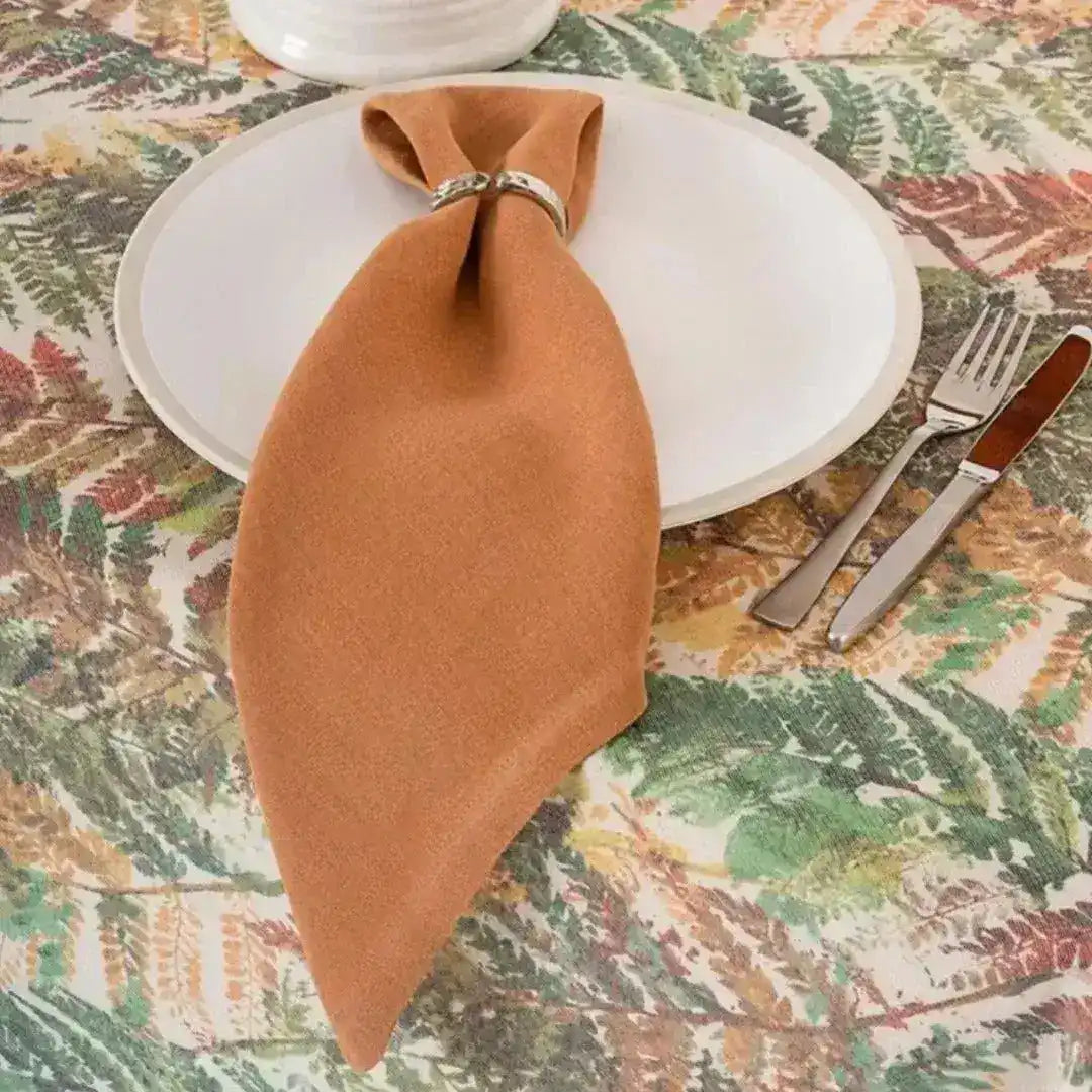 Rustic rust placemat styled as folded napkin through silver ring on white plate, botanical-print tablecloth setting
