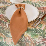 Rustic rust placemat styled as folded napkin through silver ring on white plate, botanical-print tablecloth setting