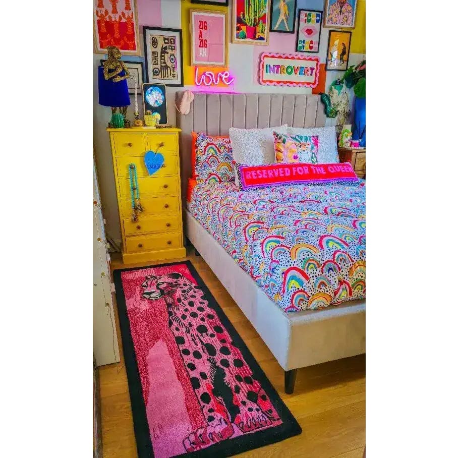 A vibrant bedroom showcasing a colorful abstract area rug with a striking leopard design placed beside a bed. The room features a lively decor with a mix of framed art, neon signs, and a bright yellow dresser, perfect for adding a contemporary touch as a hallway runner rug or wool rug in the living room.