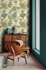 Sage ginkgo leaf wallpaper in corner with carved wood cabinet, teal vases and curved wood chair