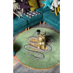 A stylish round wool rug in dark green featuring a scalloped snake design, perfect for adding a unique touch to dining rooms or bedrooms. The rug is placed in a cozy living space with teal couches and vibrant pillows, showcasing its versatility as an area rug.