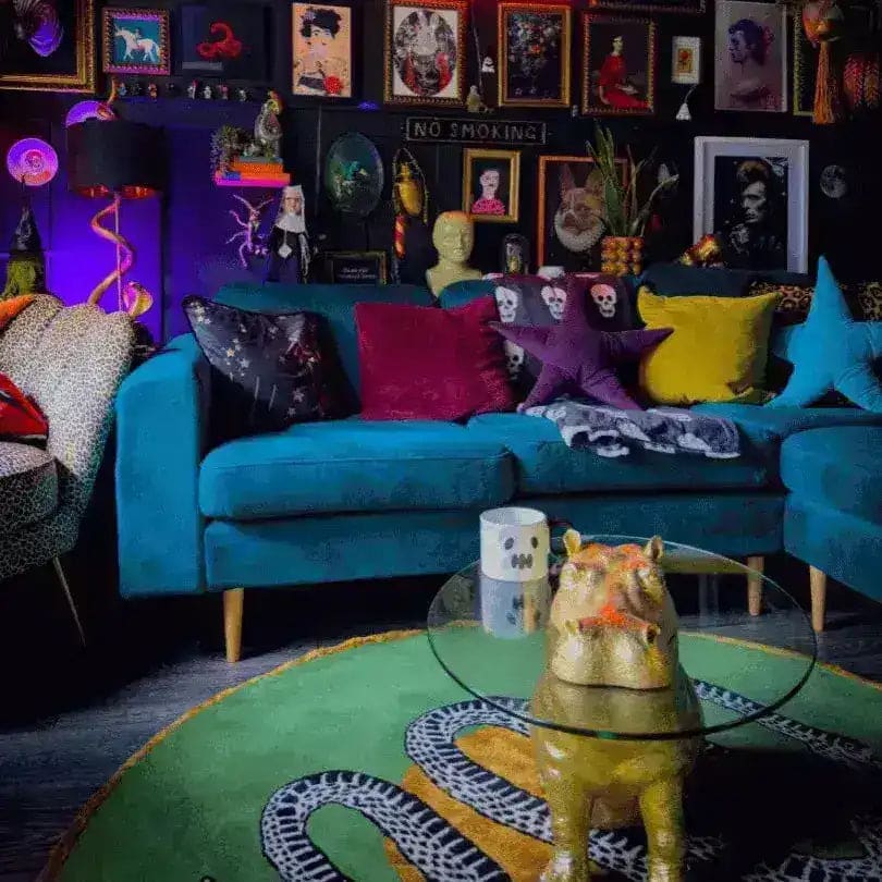 A vibrant living room features a unique round wool area rug with a scalloped green snake design, complementing the eclectic decor. The large living room rug adds a pop of color under a whimsical hippo-shaped glass table, surrounded by a blue sofa adorned with colorful cushions. The walls are decorated with an array of framed artworks, creating an artistic and cozy atmosphere.