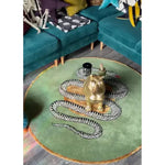 A stylish area rug in a dining room setting, featuring a scalloped green snake and apple design on a dark green wool surface. The round rug complements the teal sofas and vibrant decor, adding a touch of elegance to the bedroom or living area.