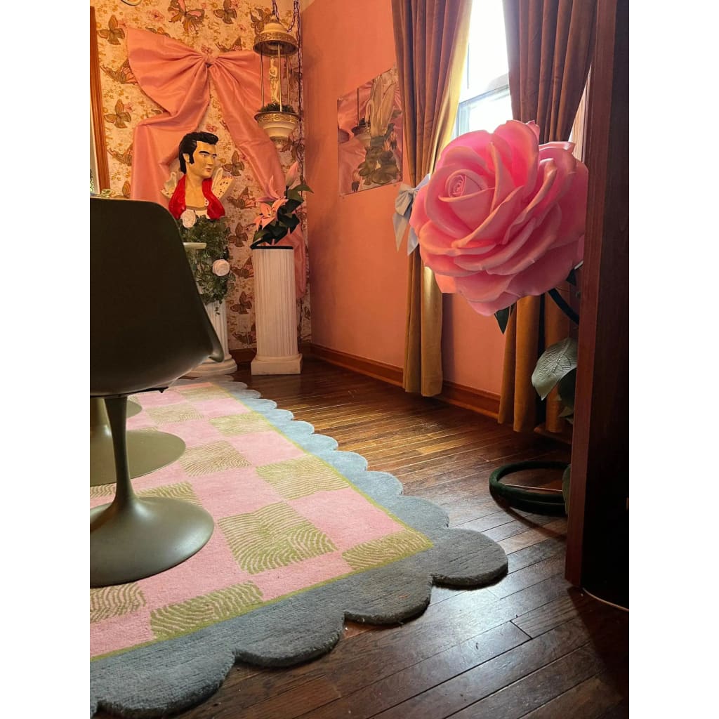A cozy living room scene featuring a Scalloped Leaf Checker Pastel Hand Tufted Area Rug. This large wool rug, with its soft pink and green checker pattern, adds a boho touch to the space. Perfect for large living rooms, the rug's scalloped edges create an inviting contrast against the hardwood floor.