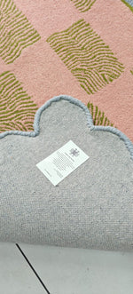 Gray rug with a textured border and a label on a pink and green patterned background