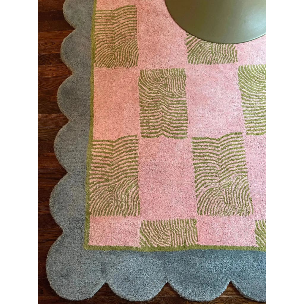 A close-up view of a Scalloped Leaf Checker Pastel Hand Tufted Area Rug, ideal for large living rooms. This wool rug features a pink and green checker design with a scalloped blue edge, perfect for adding a boho touch to your space. Its unique pattern and soft texture make it a standout among large area rugs for living rooms.