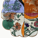 Close-up view of the Scalloped Meadow Hand Tufted Round Rug, showcasing a vibrant floral design. The area rug features a dynamic mix of orange, green, purple, and cream colors, perfect for enhancing large living rooms. This wool rug offers an artistic touch with its unique scalloped edge, making it an ideal choice for living room rugs 8x10. The intricate floral patterns add a touch of elegance to any space, combining beauty and functionality in large area rugs for living rooms.