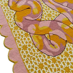Close-up of a hand-tufted area rug with a scalloped edge, featuring a vibrant serpentine pattern in shades of pink, orange, and yellow. Ideal for both bedroom and living room, this wool rug adds a touch of elegance and warmth to any space.