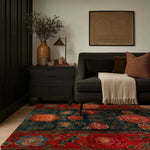 A cozy living room featuring a Scarlet Blossom Heritage Hand Tufted Area Rug. This vibrant floral rug adds elegance to the space with its bold red and blue floral patterns, perfect for dining room carpets. The wool rug complements the dark sofa and warm tones, making it ideal for both living room and dining room settings.