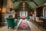 Luxurious living room with floral runner rug, stone fireplace, teal armchair, and wooden beams.
