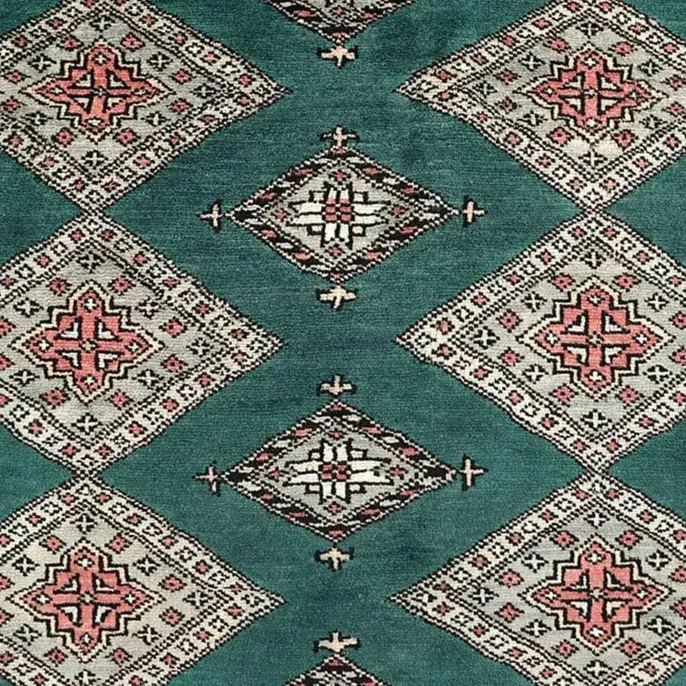 A detailed view of a Sea Green Sarong Hand Knotted Area Rug, featuring intricate geometric patterns in shades of red, white, and black. This elegant large living room rug showcases a series of diamond shapes on a sea green background, perfect for adding a touch of sophistication to any space.