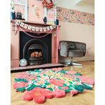 A vibrant floral round area rug in a cozy living room setting. The wool rug features bold pink and green flowers, adding a splash of color to the parquet floor. Perfect as an 8x10 living room rug, it complements the charming decor, including a pink fireplace adorned with whimsical decorations.
