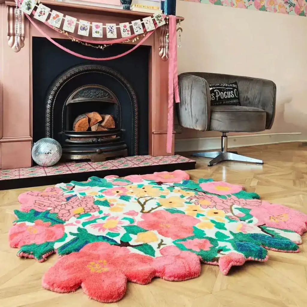 A vibrant floral round rug placed in a cozy living room setting, showcasing the Secret Garden Hand Tufted design. The wool rug features bold pink and green floral patterns, perfect for adding a splash of color and style as a living room rug. This area rug complements the surrounding decor, including a vintage fireplace and a comfortable gray chair, ideal for an 8x10 space.