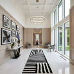 Modern interior hallway with a black and white striped rug, wall art, and large windows.