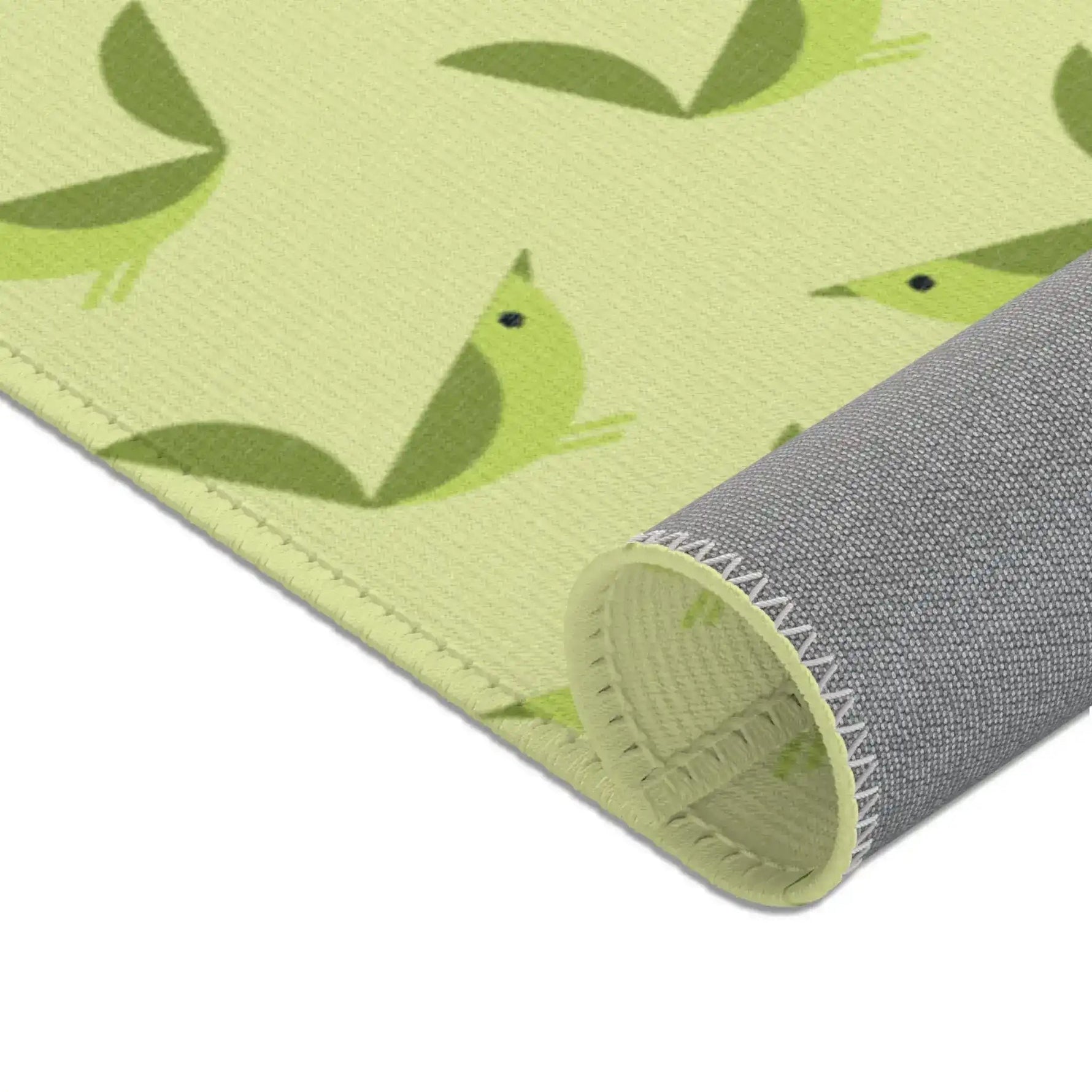 Serene songbird rug rolled at corner, close green bird motifs and gray backing on celery ground
