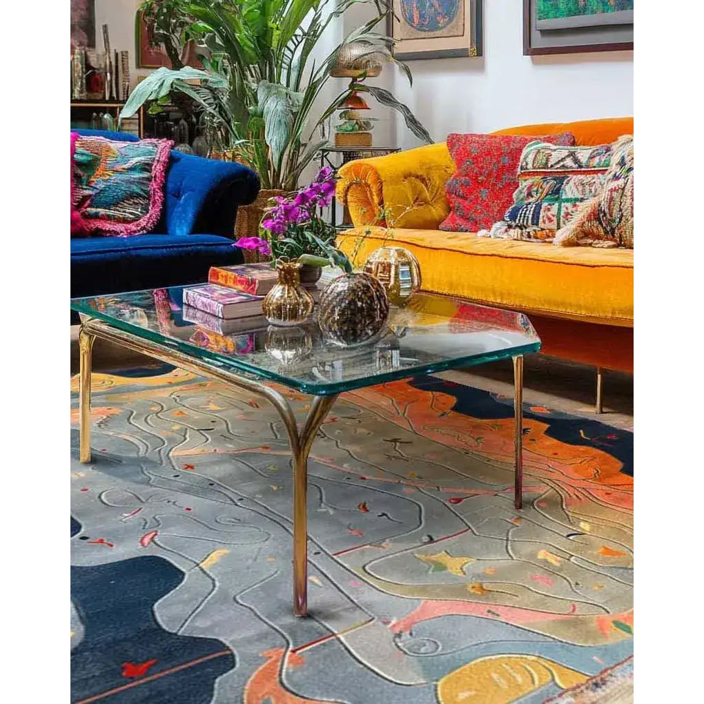 A vibrant contemporary area rug in a dining room setting, showcasing a wool texture with abstract patterns in blue, orange, and gray tones. The large area rug complements the colorful couches and glass-top table, creating a lively and inviting atmosphere ideal for a dining table rug or dining room carpet.