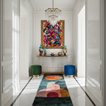 Colorful abstract painting on a wall above a colorful rug in a modern hallway.