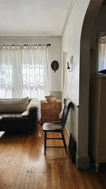 Sheepskin pelt rug on gray sofa in bright living room with pine dresser, sheer curtains, arched doorway, wood floor