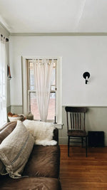 White sheepskin pelt rug tossed over brown leather sofa back in living room with wooden chair and curtained window
