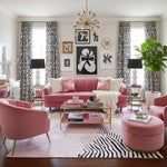 Living room with pink sofa, armchairs, and ottoman, featuring a pink abstract wool rug, decorative elements and artwork.