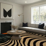 A contemporary area rug with bold, sleek stripes is featured in a stylish living room setting. The wool rug enhances the modern aesthetic of the room, which includes a comfortable grey sofa, a round wooden coffee table, and a large window letting in natural light. Ideal for dining rooms or office spaces, this eye-catching rug adds a touch of elegance and warmth.