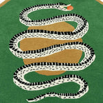 A stylish round wool area rug featuring a striking snake and apple design on a green background, perfect for enhancing a formal dining room setting. This large area rug adds a touch of elegance to dining room decor.