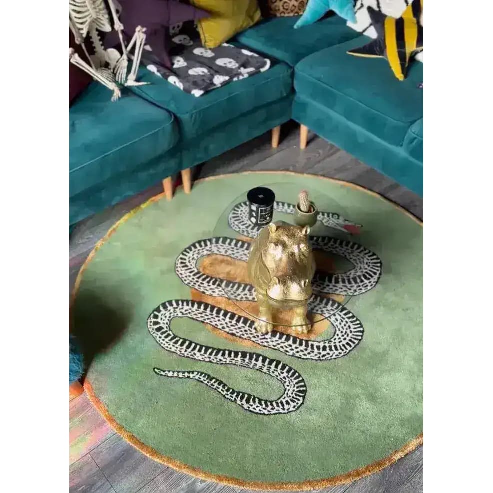 Top view of a stylish round wool rug in a dining room setting, featuring an intricate snake and apple design on a green backdrop. This elegant area rug complements the surrounding teal furniture, making it an ideal choice for formal dining room decor.