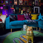 Cozy living room featuring a vibrant blue sofa adorned with colorful pillows and a unique Snake and Apple Round Hand Tufted Wool Rug. The round rug adds a playful touch to the space, perfect for those looking for stylish living room area rugs. This wool rug beautifully complements the eclectic decor with its artistic snake design, creating an inviting atmosphere.