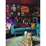 A stylish dining room showcasing a Snake and Apple Green Gold Round Hand Tufted Wool Rug. The large area rug features an intricate snake design, complementing the eclectic decor of the formal dining room. Surrounded by vibrant teal and mustard pillows on a cozy sofa, the round rug adds a unique touch to the room's ambiance.