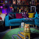 Snake and apple round rug beneath a glass coffee table beside a teal velvet sofa, room view