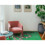 A contemporary area rug featuring a striking snake and sun design, hand-tufted in wool, perfect for adding a modern touch to a living room. This vibrant green rug is showcased in a stylish setting with a pink chair, a round coffee table, and lush indoor plants.