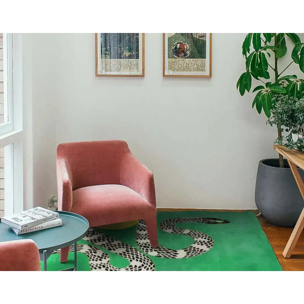 A contemporary area rug featuring a striking snake and sun design, hand-tufted in wool, perfect for adding a modern touch to a living room. This vibrant green rug is showcased in a stylish setting with a pink chair, a round coffee table, and lush indoor plants.