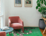 A contemporary area rug featuring a striking snake and sun design, hand-tufted in wool, perfect for adding a modern touch to a living room. This vibrant green rug is showcased in a stylish setting with a pink chair, a round coffee table, and lush indoor plants.