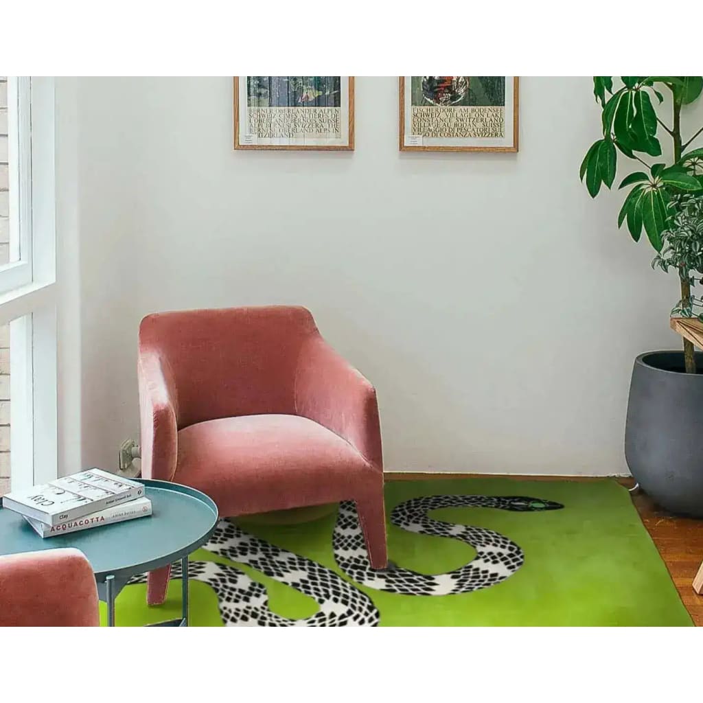 A stylish living room featuring a Snake and Sun hand-tufted wool rug in moss green. The contemporary area rug, ideal for living room rugs 8x10, showcases a bold black and white snake design against a vibrant green background. This large area rug adds a modern touch to the room, complementing the pink armchair, blue table, and indoor plant, creating a cozy and inviting space.