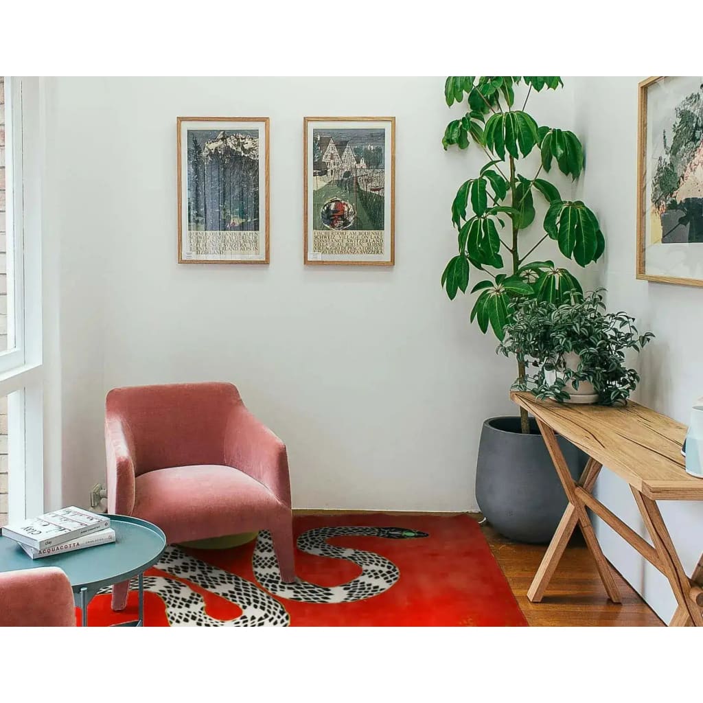 A stylish living room featuring a vibrant red hand-tufted wool rug with a snake and sun design. This contemporary area rug in a spacious 8x10 size adds a bold touch to the room, complementing the pink chair and wooden furniture. Ideal for those seeking unique rugs for living room decor.