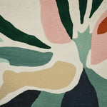 Close-up of a rug with abstract leaf pattern in green, pink, beige, and black.