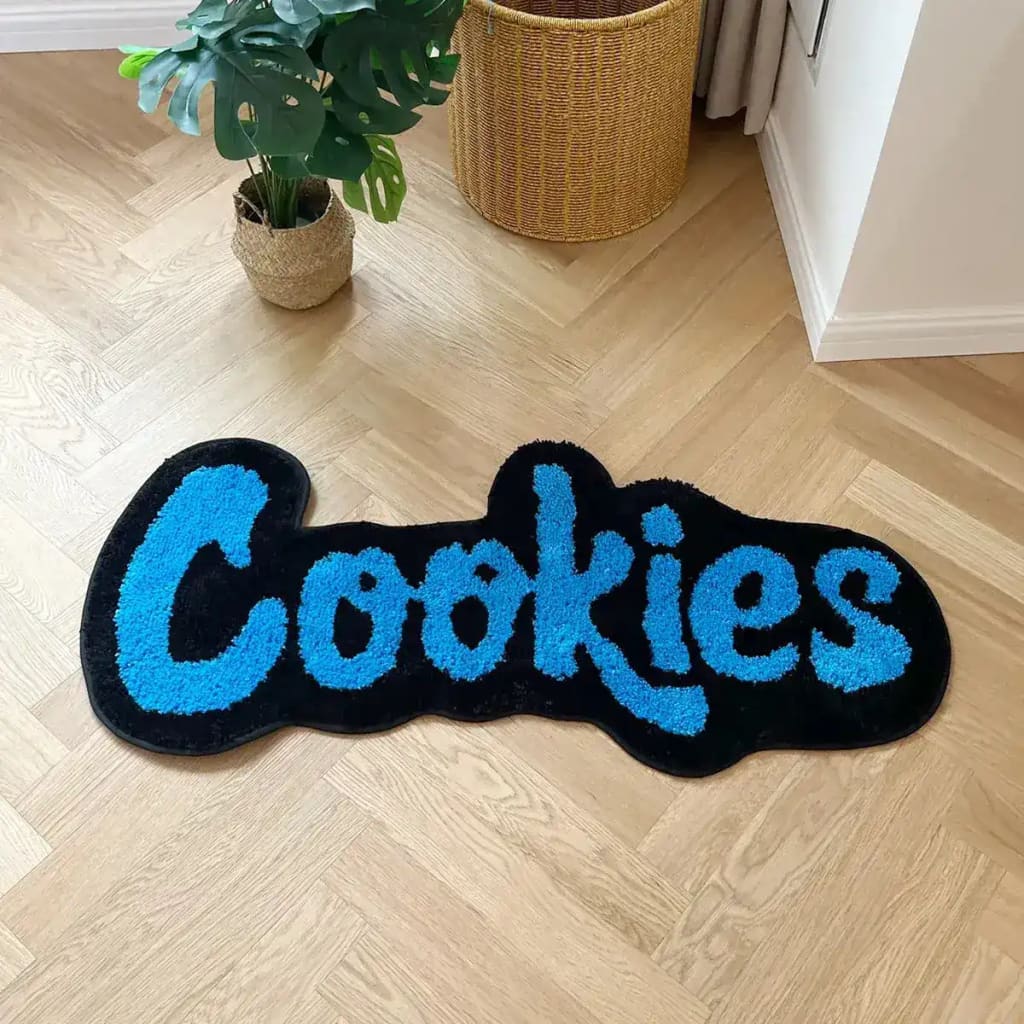 Soft Plush Handmade Cookies Bath Rug on a wooden floor, showcasing a playful design perfect for large living room areas. The area rug spells 'Cookies' in vibrant blue letters on a black background, adding a fun touch to any space.