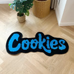Soft Plush Handmade Cookies Bath Rug on a wooden floor, showcasing a playful design perfect for large living room areas. The area rug spells 'Cookies' in vibrant blue letters on a black background, adding a fun touch to any space.