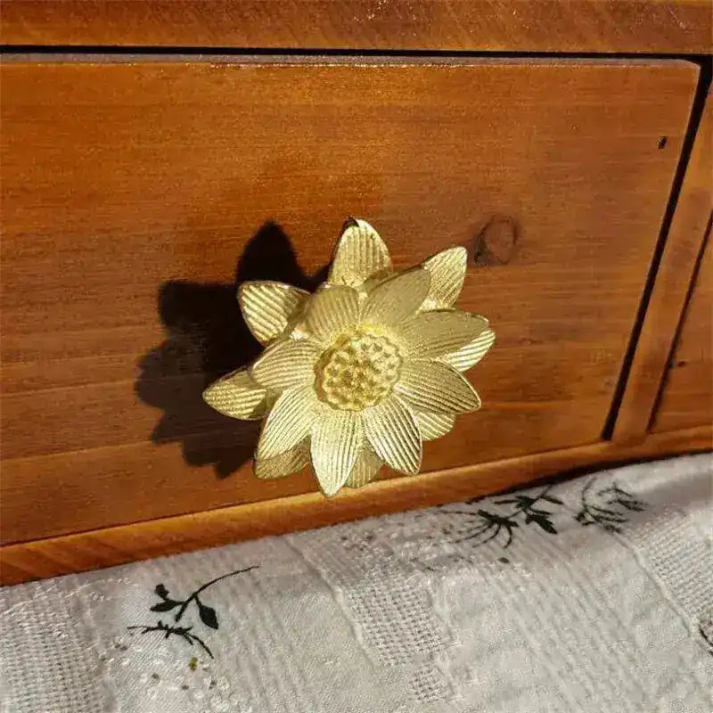 Brass lotus floral cabinet knob on wood drawer front, angled view with botanical fabric below