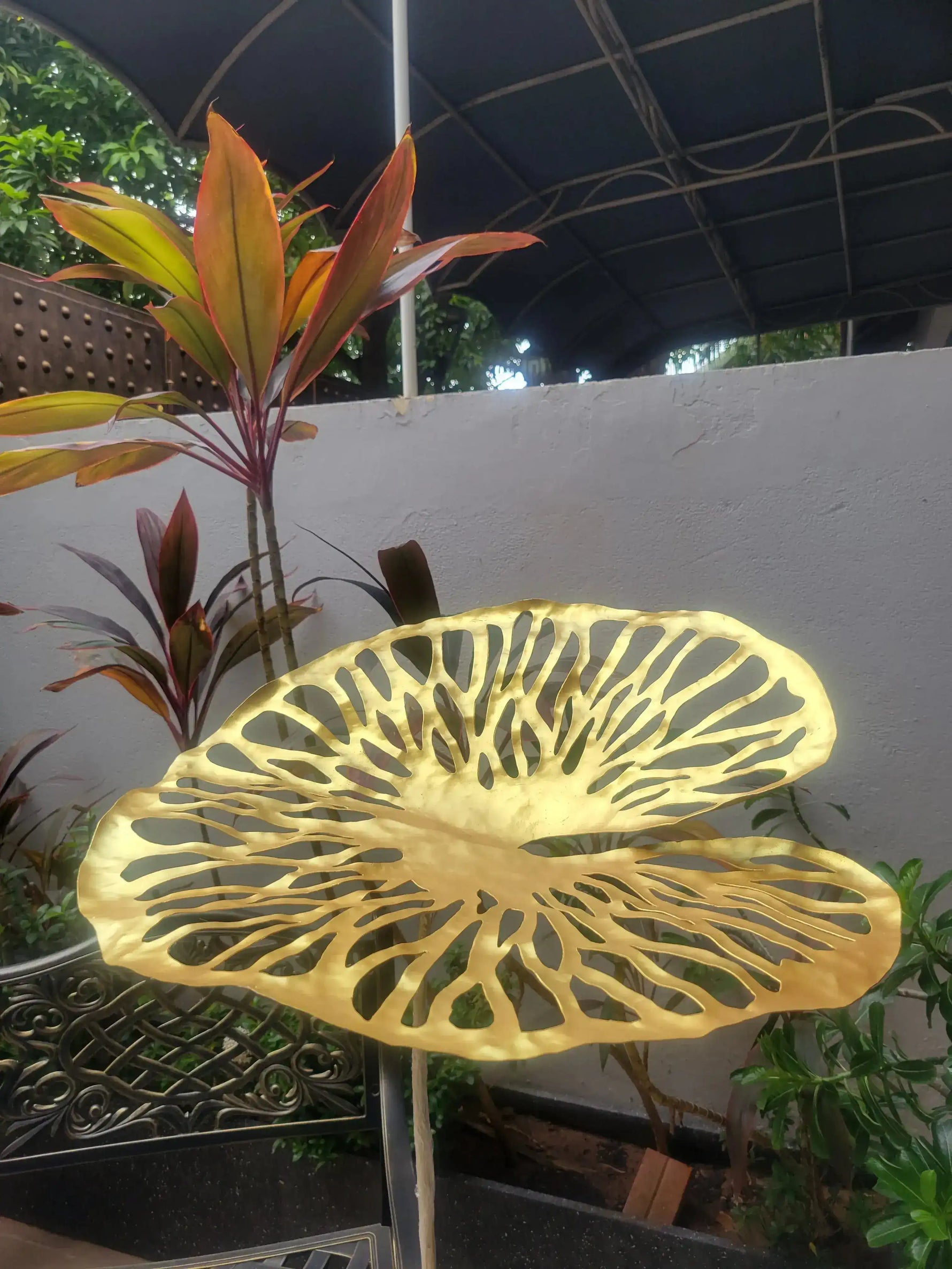 Two gold brass lotus leaf discs with cutout vein pattern atop a slim stem, photographed at night with tropical foliage and warm light