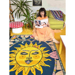 A vibrant area rug with a sun motif, part of the Solstice Dreams collection, adds warmth and style to a living room. This wool rug features bold yellow and blue tones, perfect for elevating any space with its artistic design.